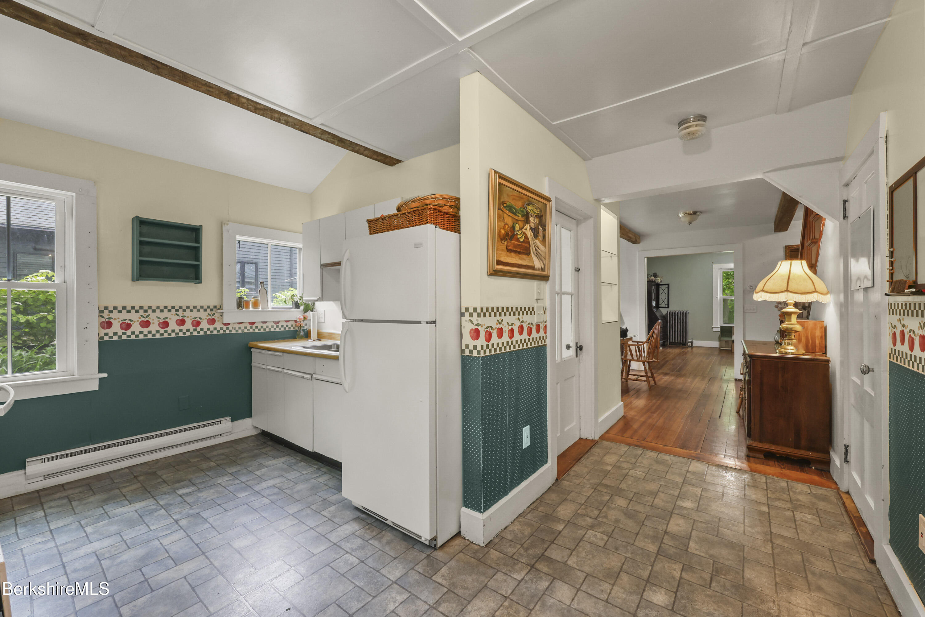 Kitchen with green apple-patterned tile trim, white refrigerator, and a view into a wood-floored room.