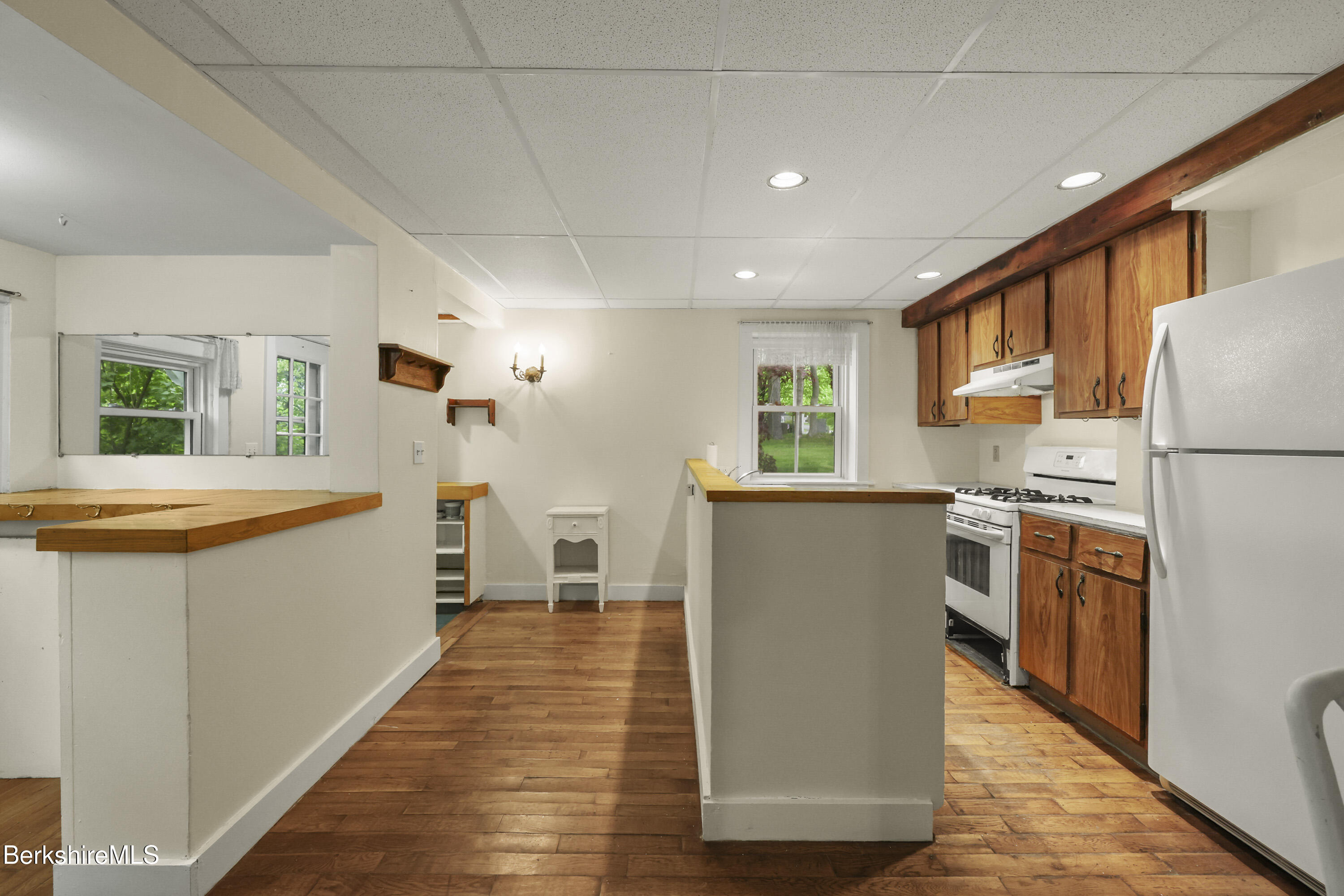 Kitchen with wood cabinets, plank flooring, a breakfast counter, and white appliances.