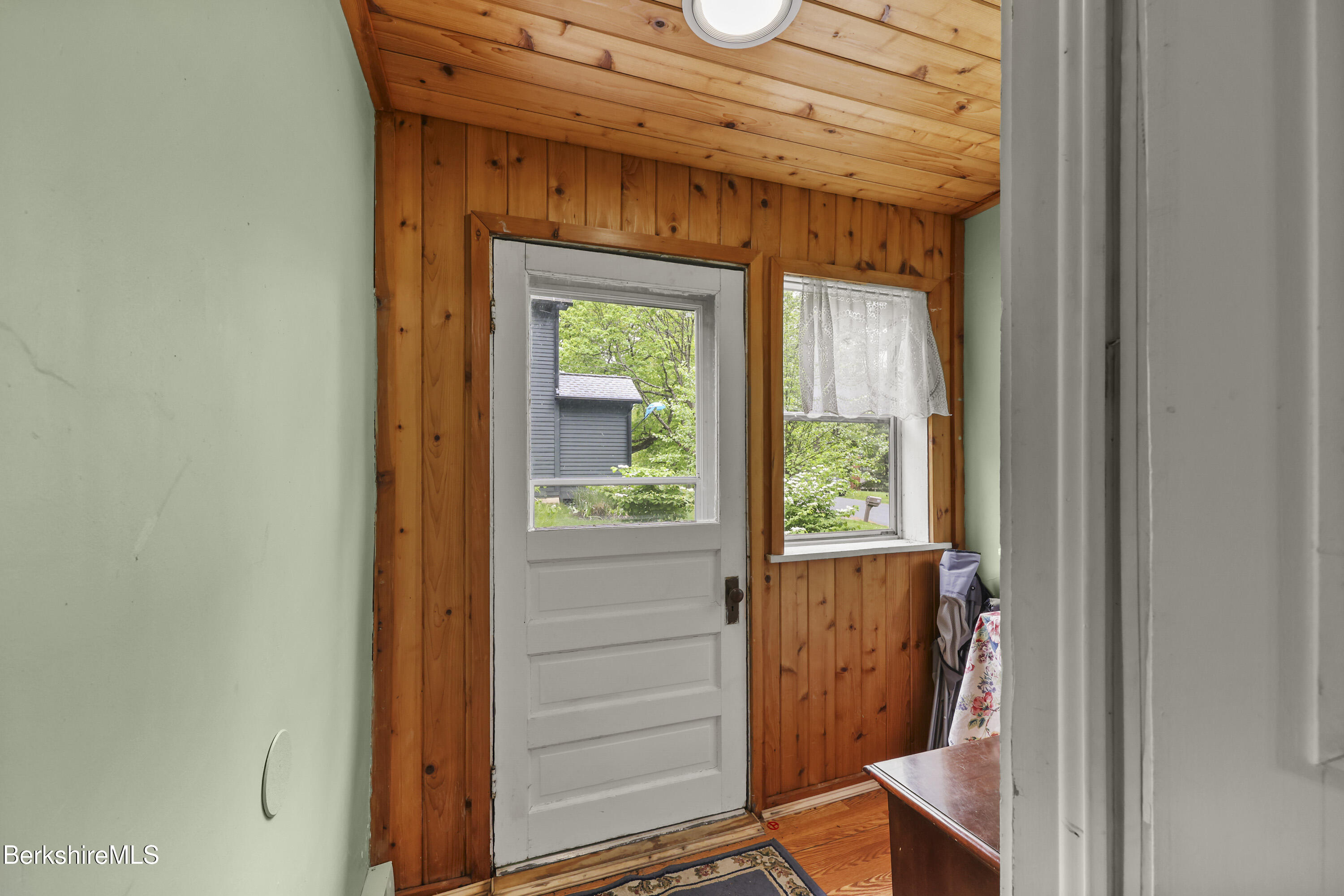 Entryway with a white paneled door, window, and warm wood-paneled walls and ceiling.
