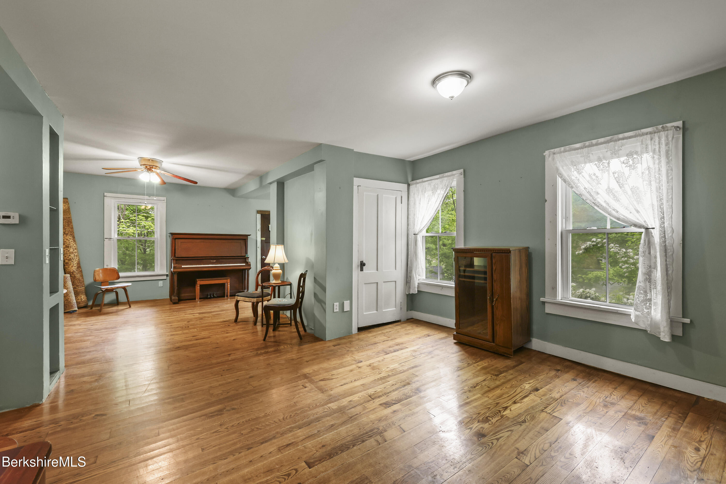 Living room with an upright piano, sage-green walls, and polished hardwood floors.