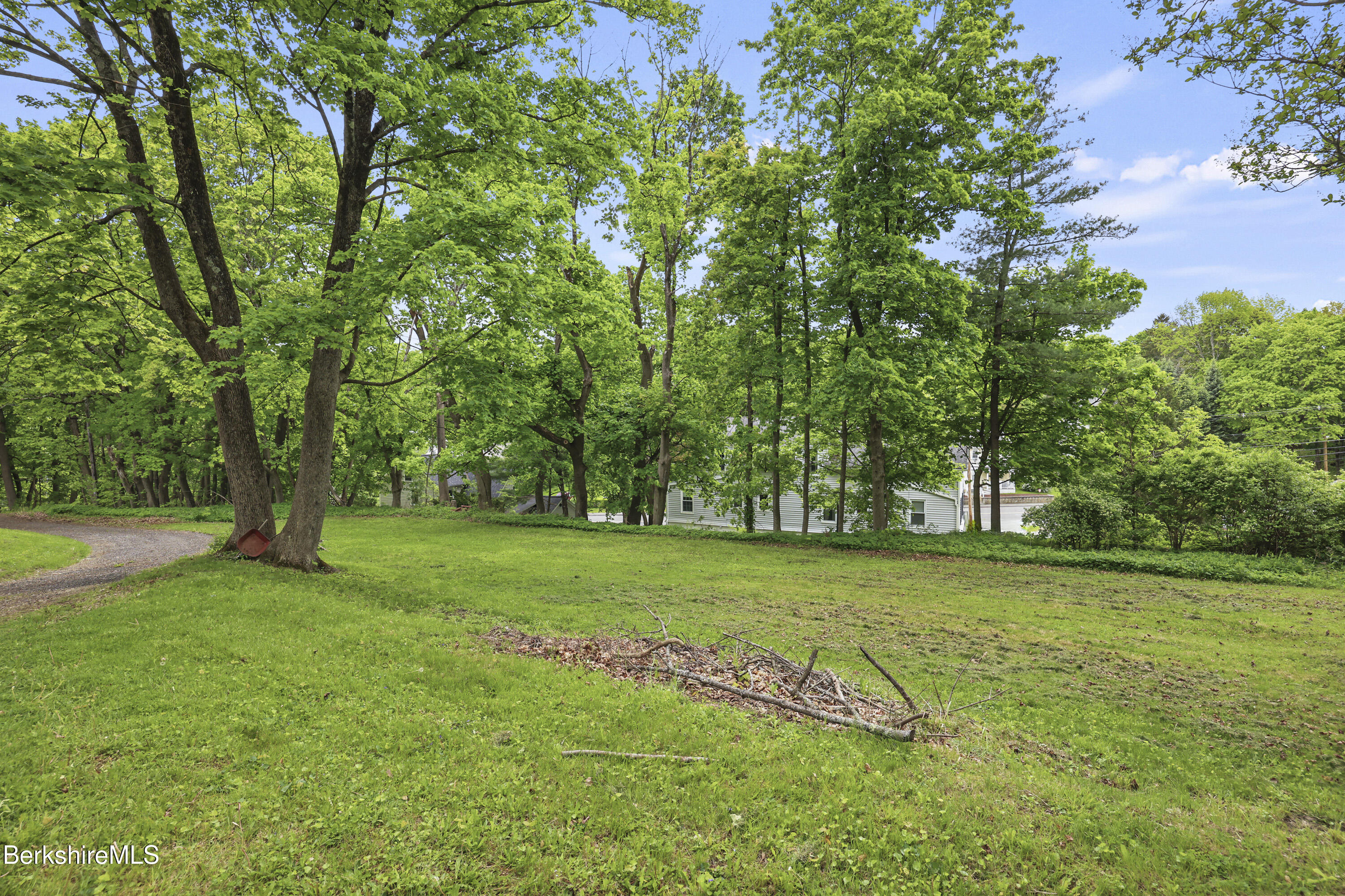 Tree-shaded lawn with a curved gravel path and a white house partly visible through mature trees.