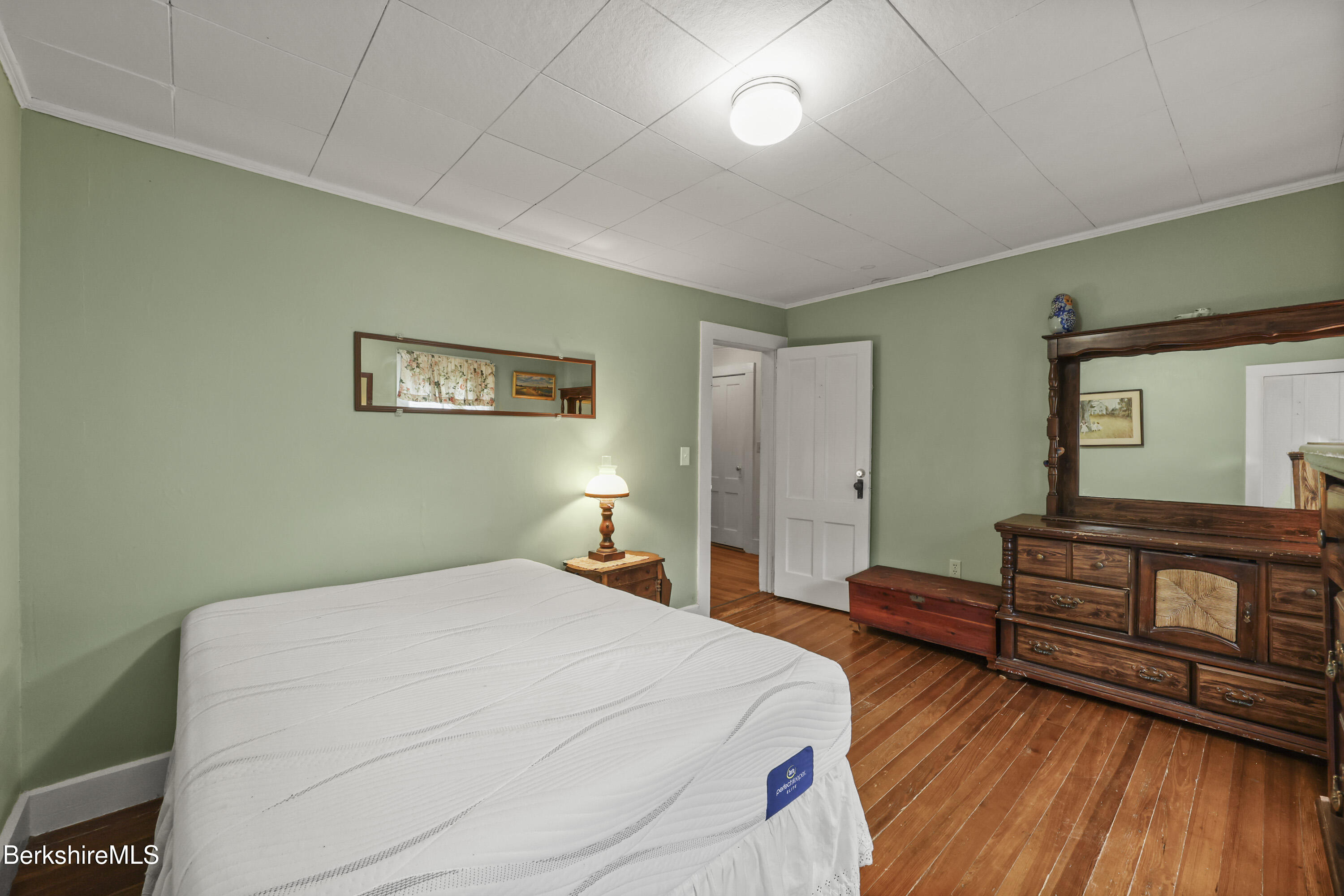 Bedroom with sage-green walls, hardwood floors, a white mattress, and a large wooden dresser.