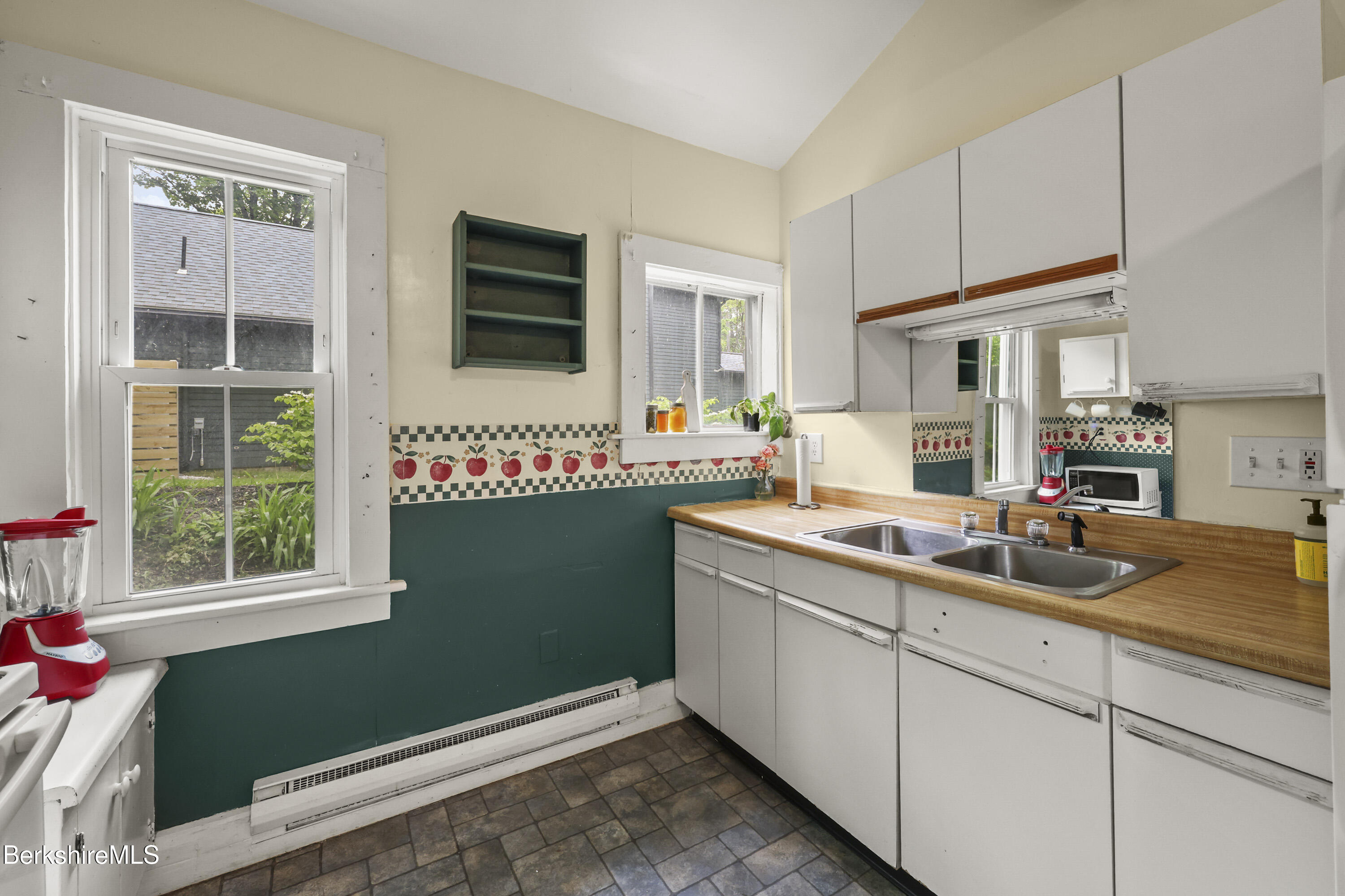 Kitchen with white cabinets, wood countertops, double sink, and apple-pattern backsplash.