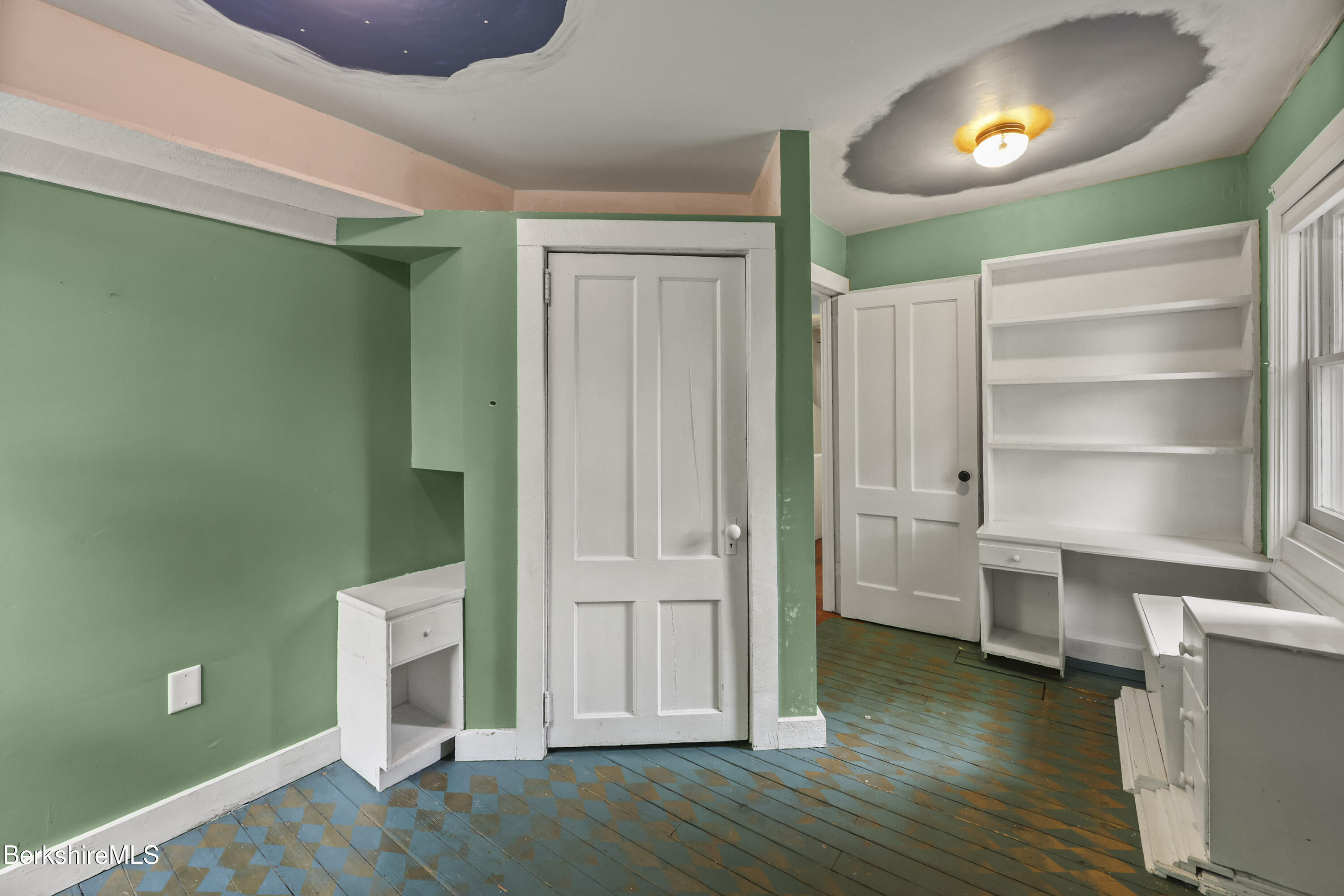 Room with green walls, blue patterned wood flooring, and white built-in shelves.