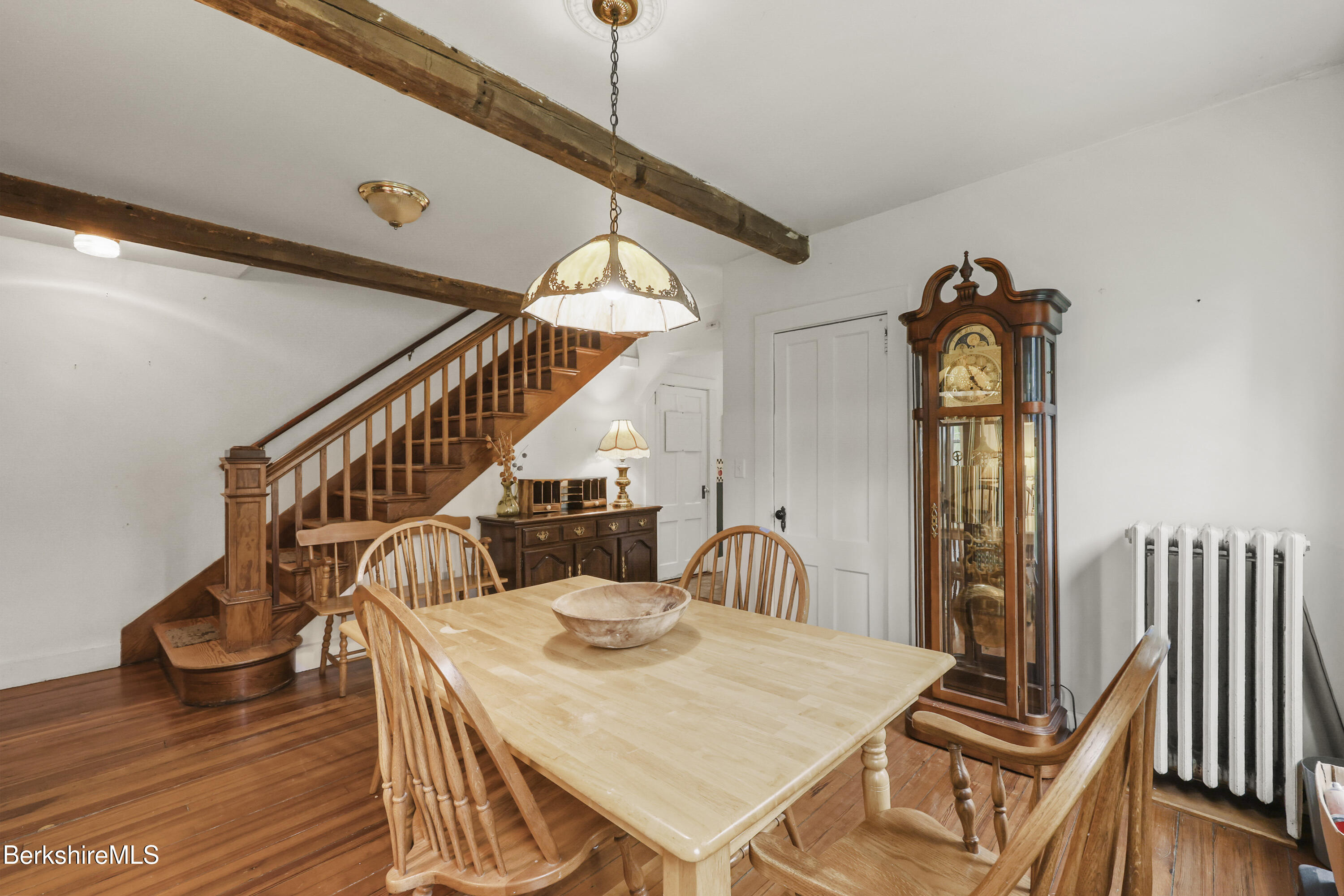 Dining room with exposed beams, a wooden staircase, and a grandfather clock beside the dining table.