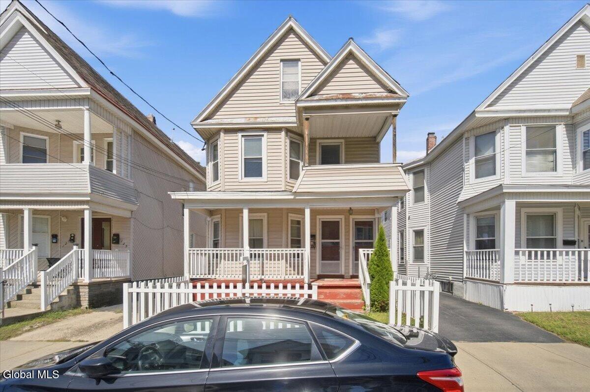 Beige two-story house with a covered porch and white picket fence, seen from the street.