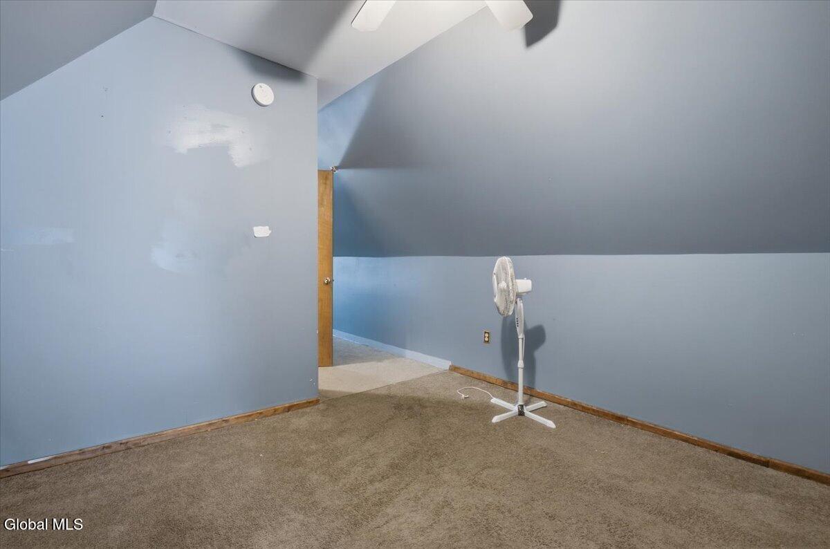 Empty blue room with a sloped ceiling, brown carpet, and a standing fan.