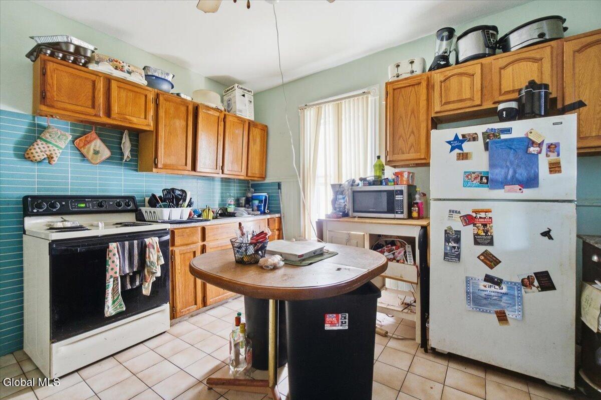 Kitchen with wood cabinets, teal tile backsplash, white appliances, and a central table.