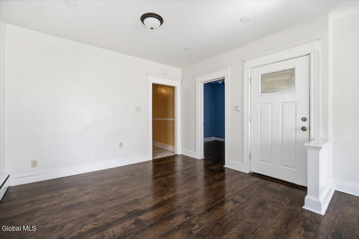 Vacant entry area with dark wood floors, a white front door, and open doorways to amber and blue rooms.