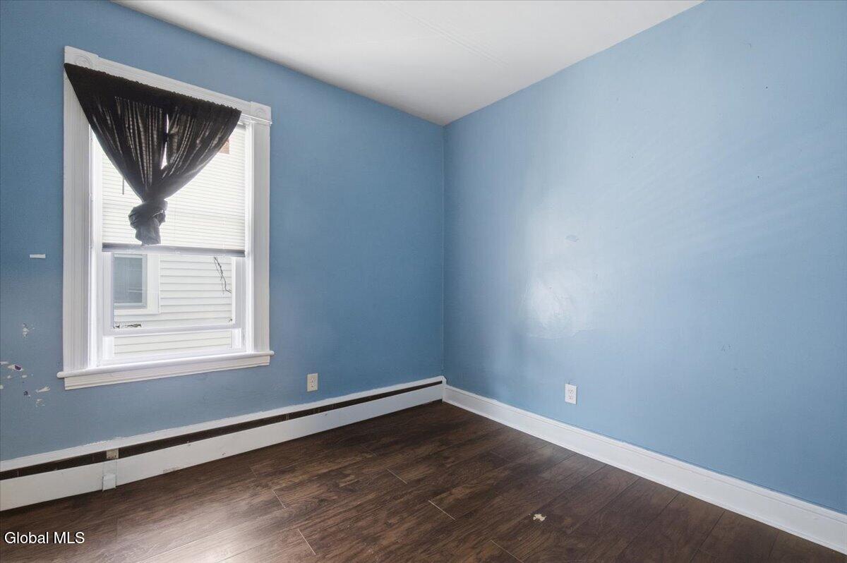 Empty room with blue walls, dark flooring, a window, and a baseboard heater.