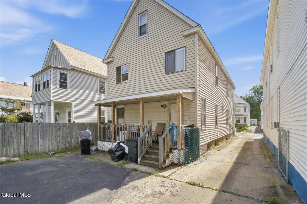 Rear of a two-story beige house with a covered porch and paved driveway.