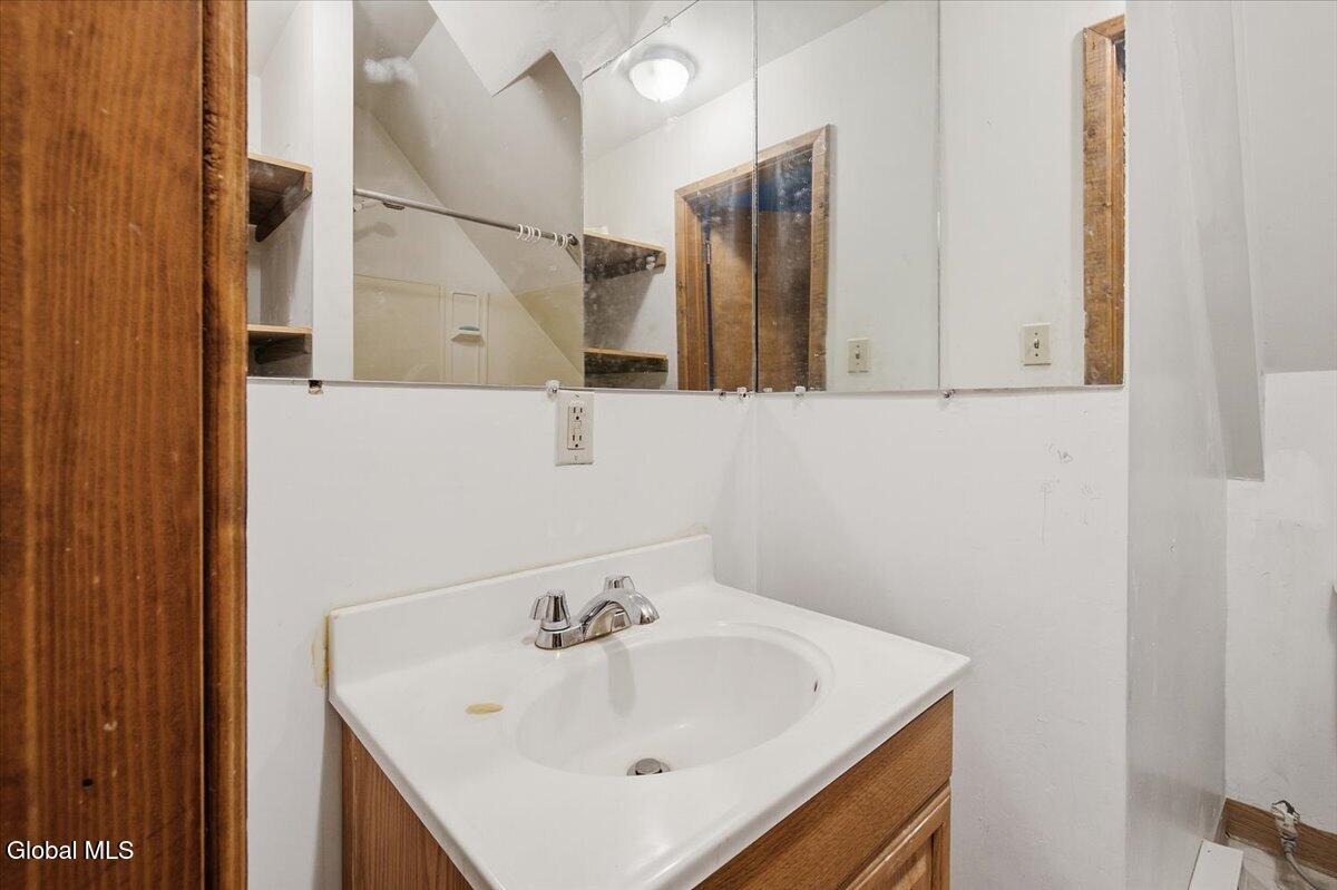 Bathroom vanity with a white sink, wide mirror, and shower reflected behind it.