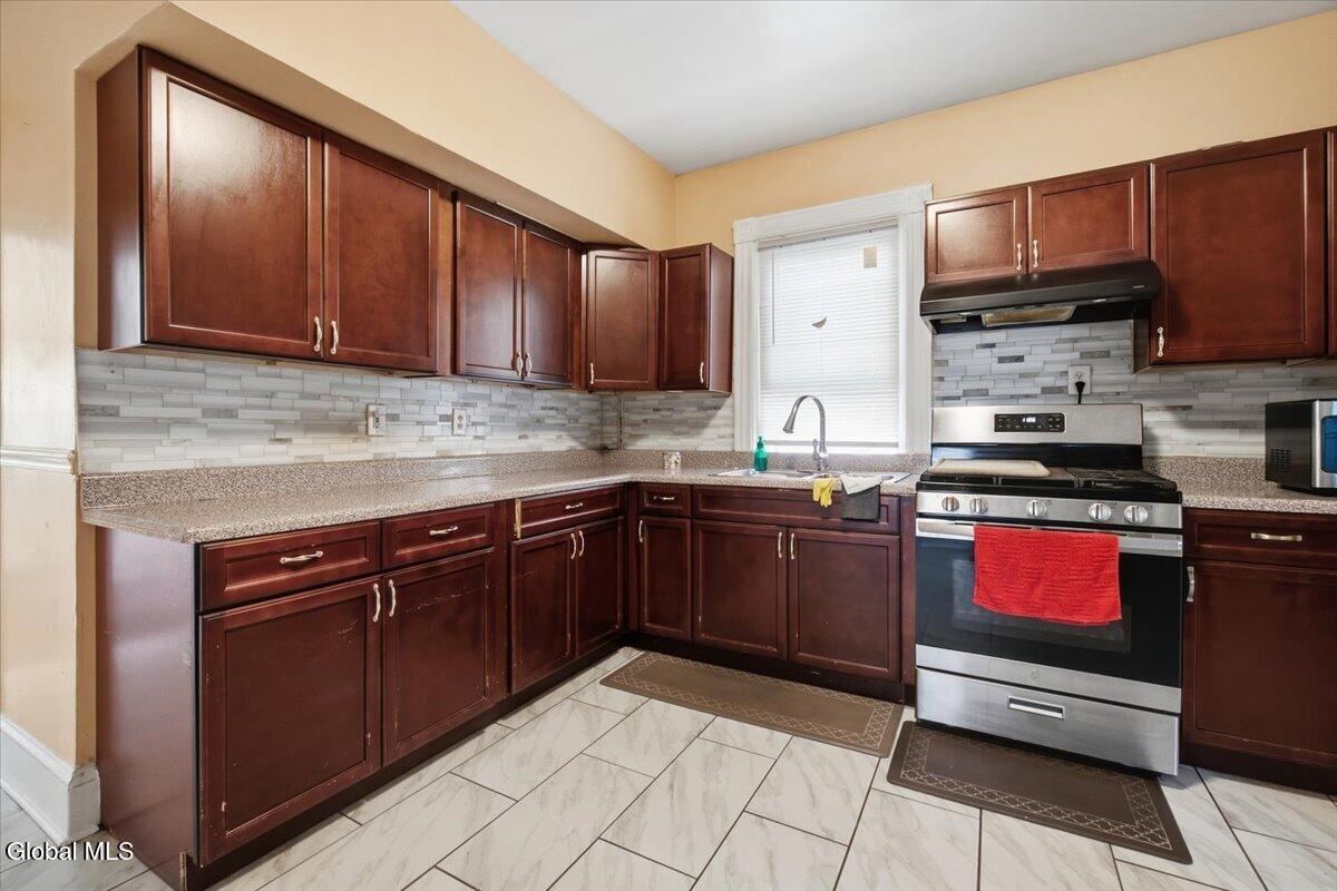 Kitchen with dark cherry cabinets, gray tile backsplash, and stainless steel range.