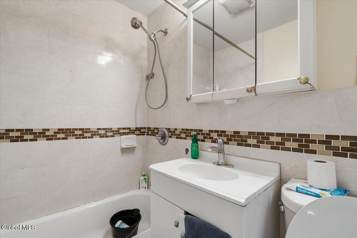 Bathroom with a bathtub and shower, white vanity, mirrored cabinet, and brown mosaic tile accent.