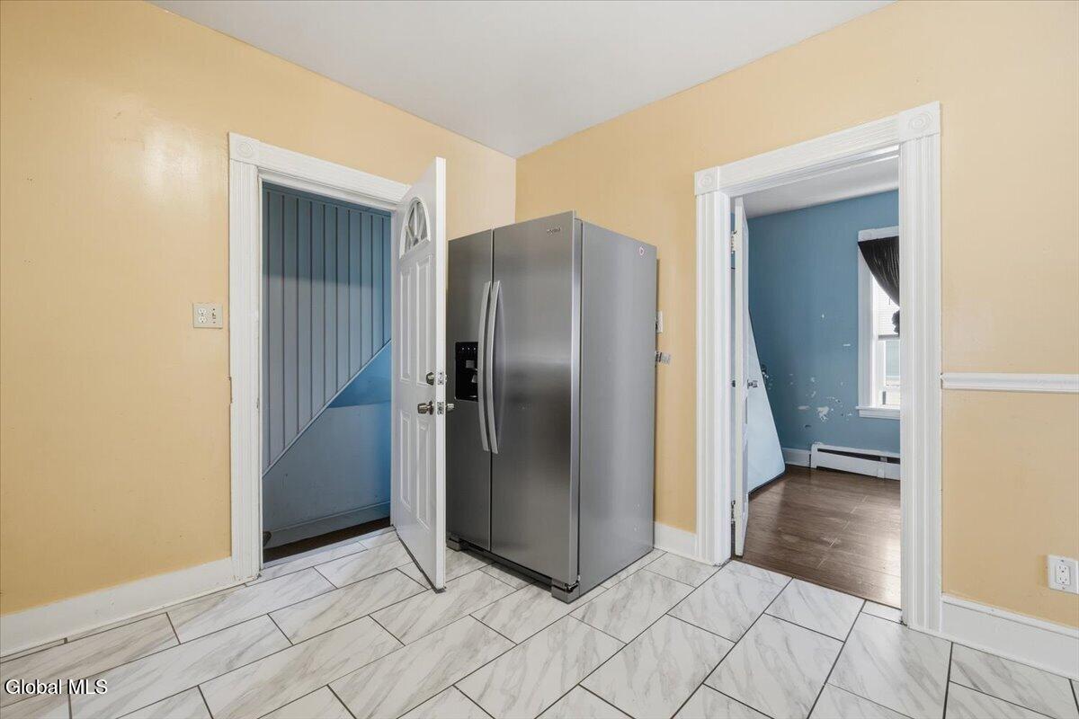 Kitchen area with a stainless steel refrigerator and marble-look tile floor beside open doorways.