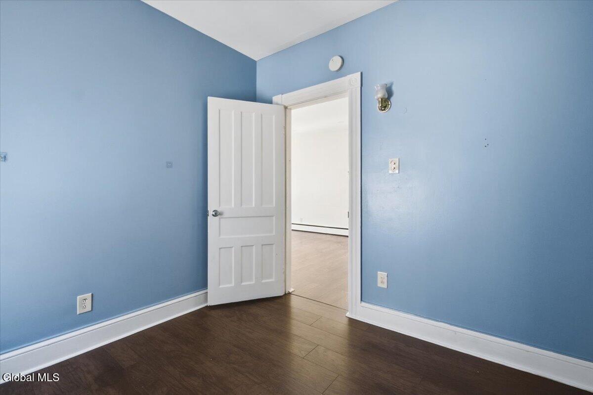 Empty blue-walled room with dark flooring and an open door to a brighter room.