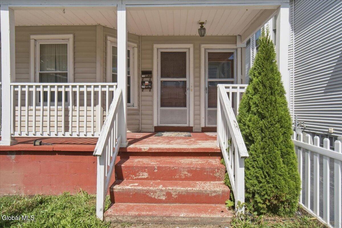 Covered front porch with red steps, white railings, and two screen doors.