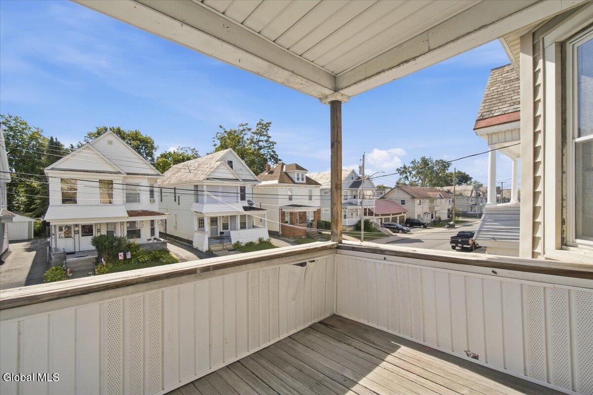 Covered porch with white railings overlooks a residential street lined with houses.