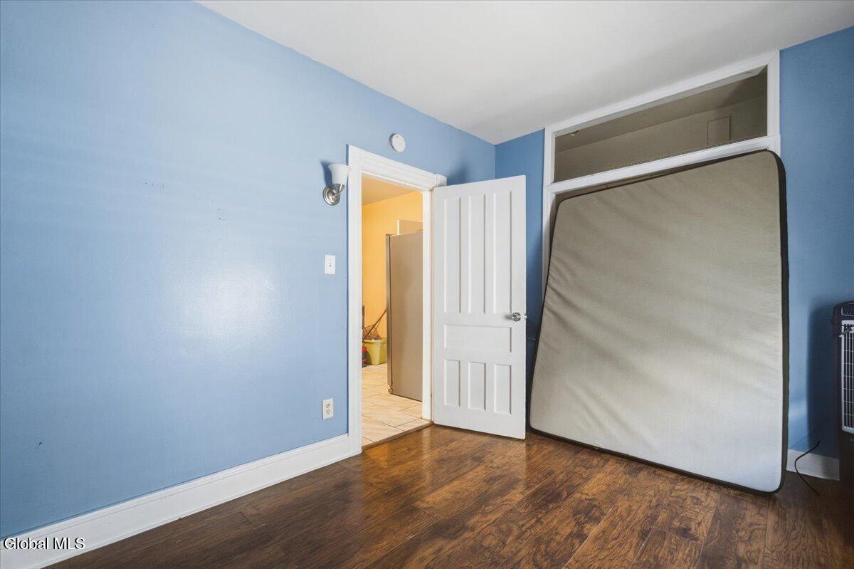 Mostly empty bedroom with blue walls, hardwood floors, and a mattress leaning against the wall.