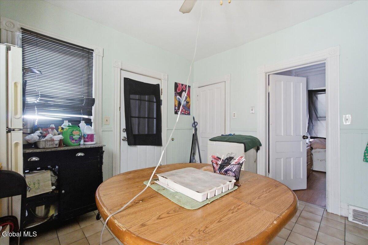 Kitchen with a round wooden table, pale mint walls, and a refrigerator beside a window.