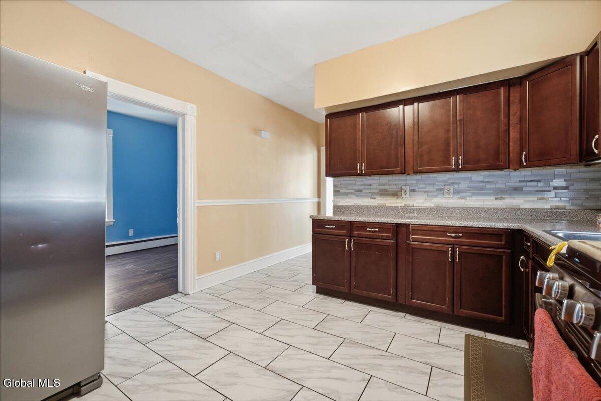 Kitchen with dark wood cabinets, a tiled backsplash, and a doorway to a blue room.