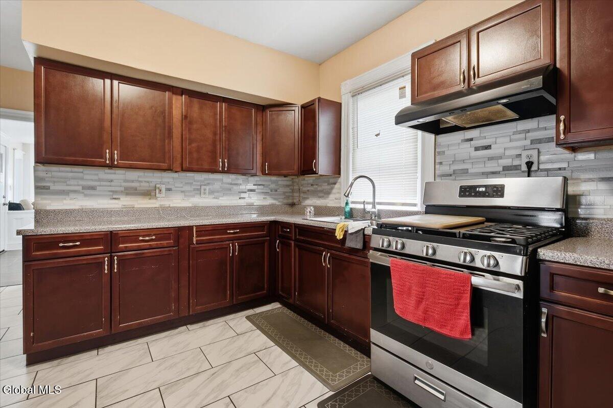 Kitchen with dark wood cabinets, a stainless steel gas range, and a gray-and-white tile backsplash.