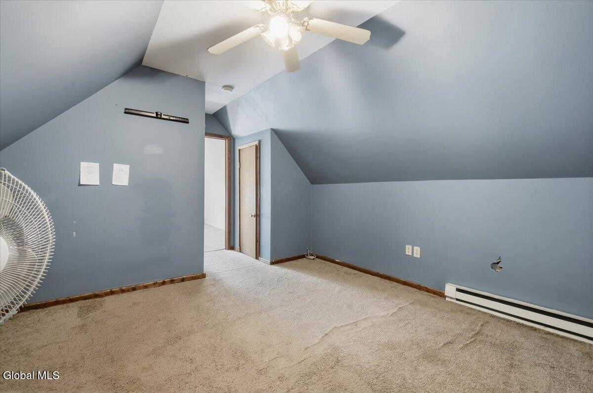 Empty carpeted room with blue-gray walls, sloped ceiling, and ceiling fan.