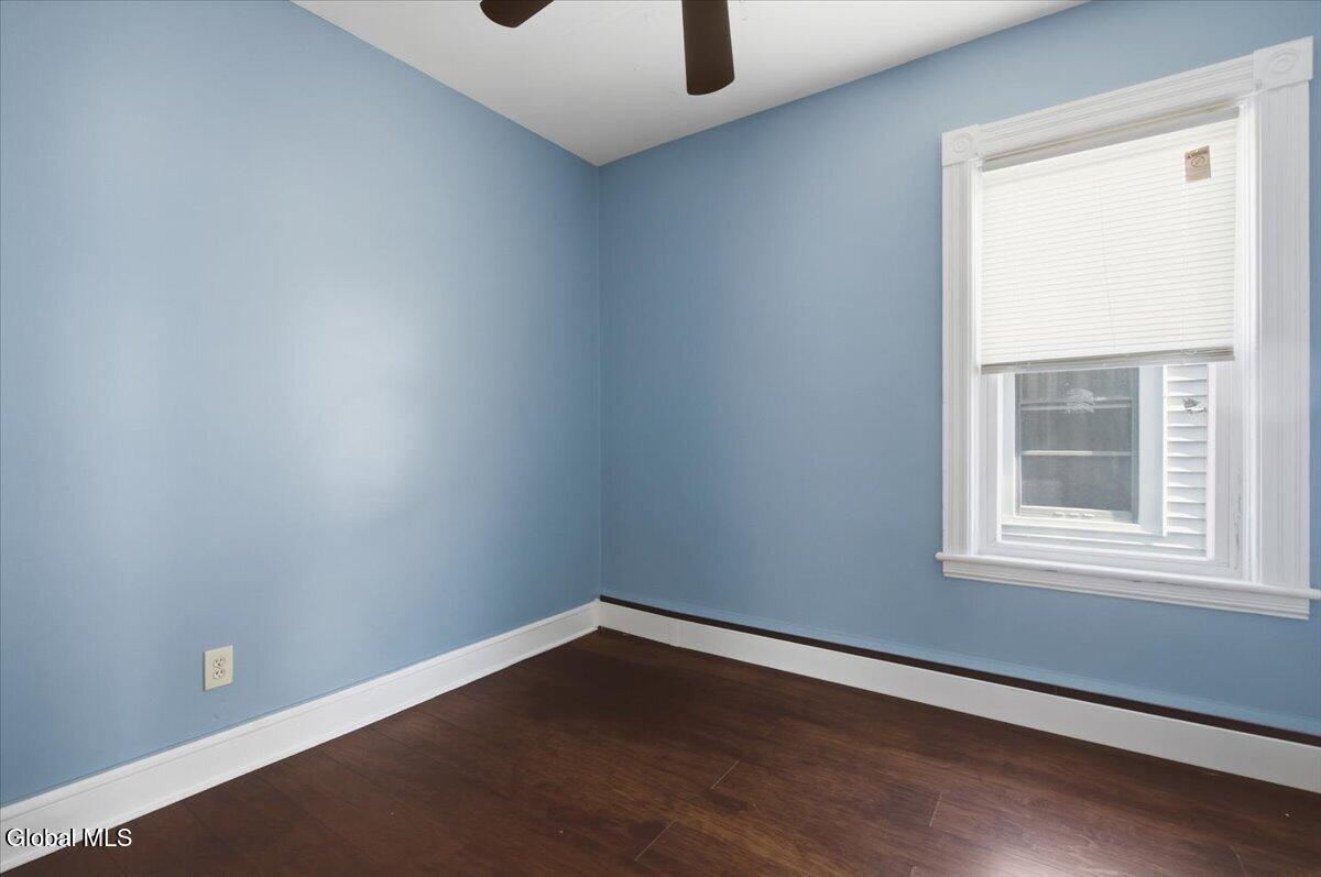 Empty blue room with dark wood flooring, white trim, and a window with closed blinds.
