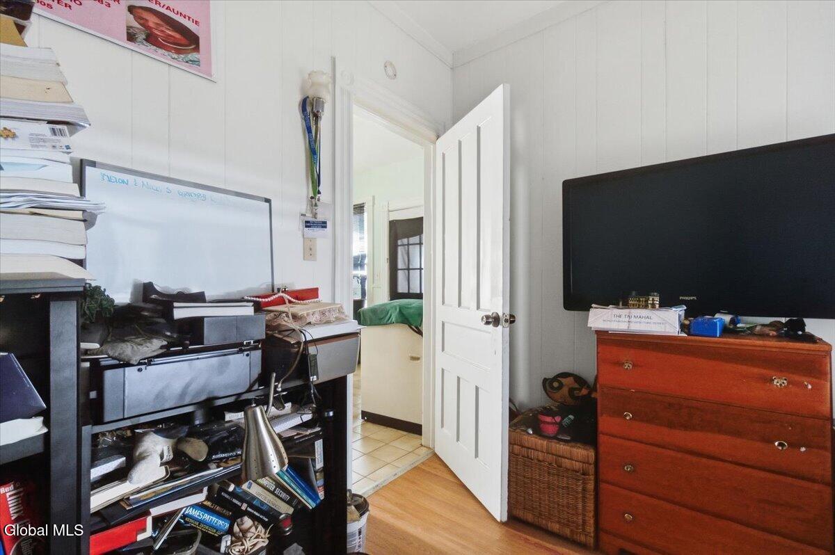 Cluttered room with crowded shelving, a whiteboard, and a television on a wooden dresser.