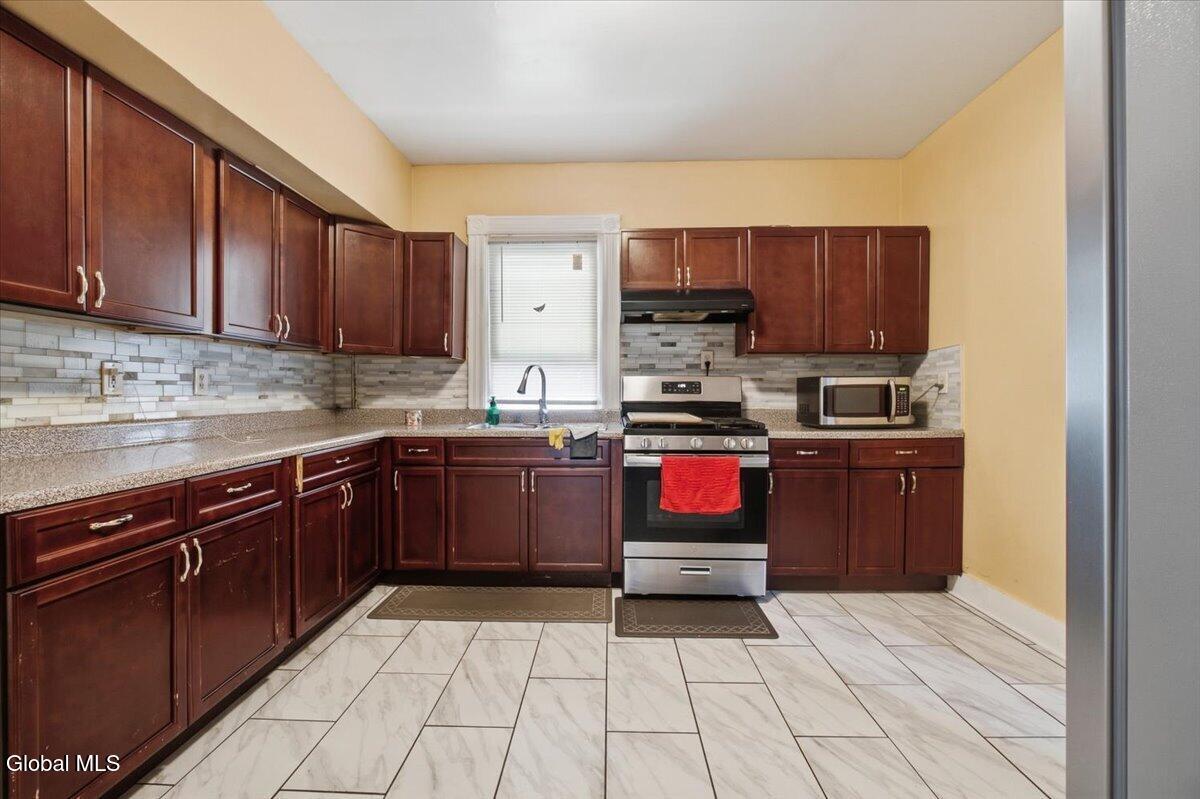 Kitchen with dark wood cabinets, tiled backsplash, stainless-steel range, and marble-look floor.