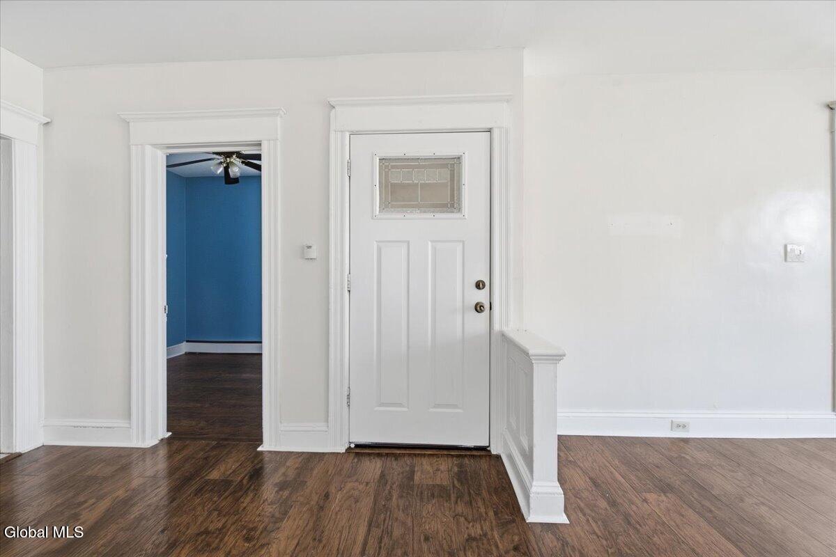 Entryway with dark hardwood floors, white trim, and a front door beside a blue room.