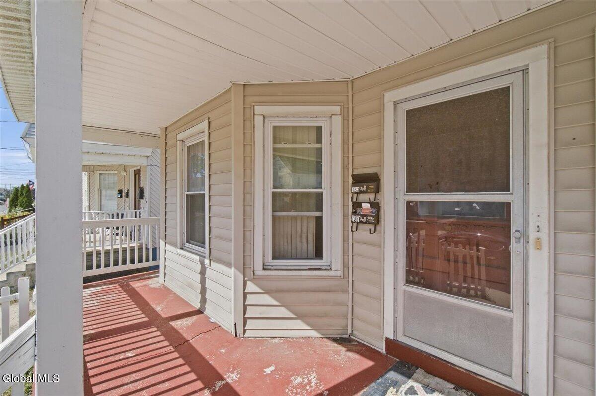 Covered front porch with a screen door, beige siding, and a weathered red-painted floor.