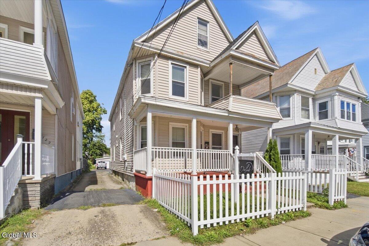 Beige two-story house with a covered porch, white railings, and a white picket fence.