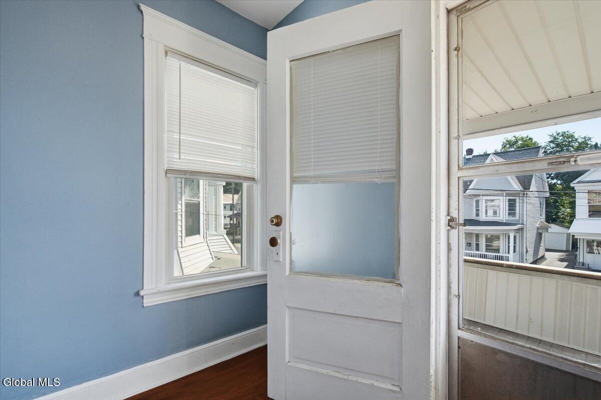 Blue-walled room with hardwood floors, window blinds, and an open door to a covered porch.
