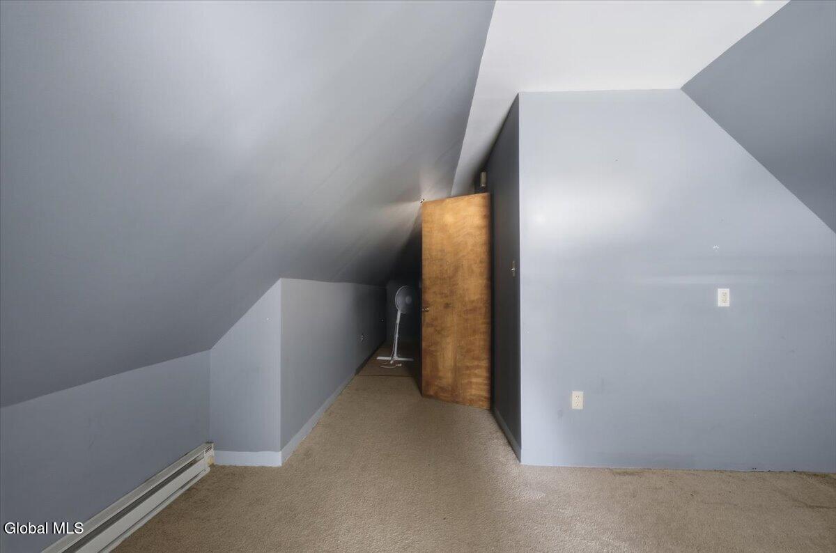Attic room with sloped gray walls, beige carpet, and a baseboard heater.