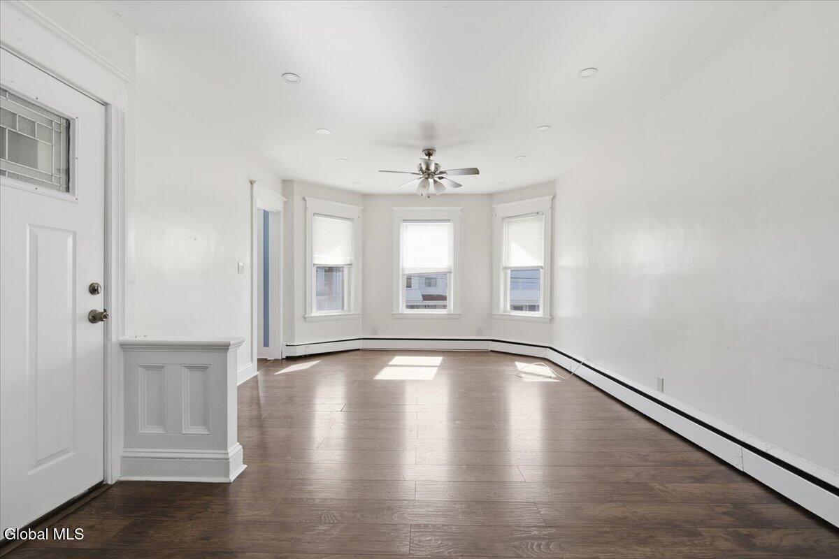 Vacant living room with dark wood floors and three bay windows.