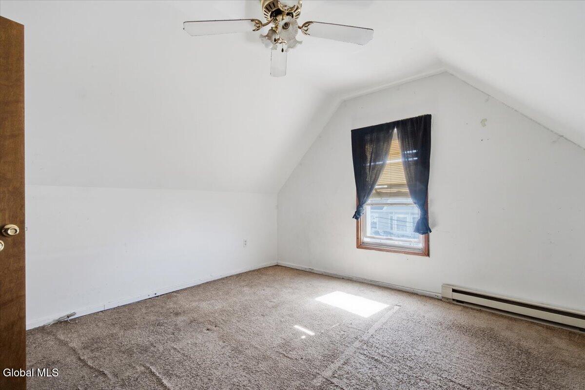Empty upstairs bedroom with sloped ceilings, beige carpet, and a curtained window.