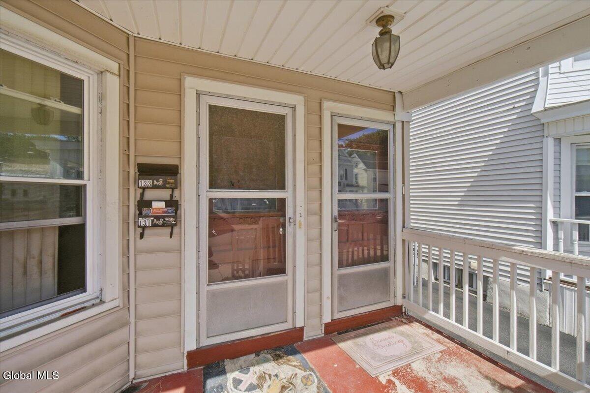 Covered front porch with two screen doors, tan siding, and white railing.