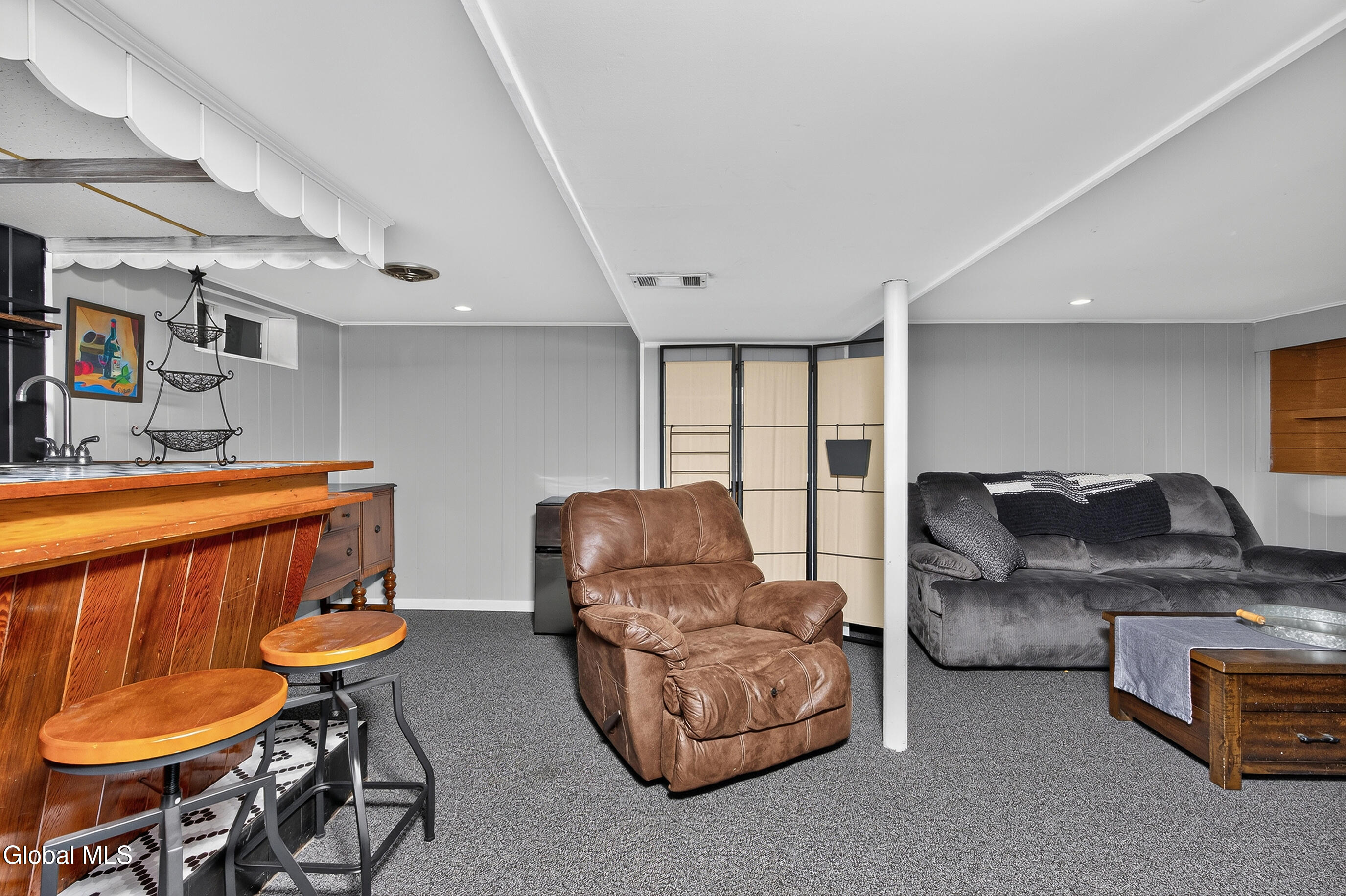 Basement lounge with a wooden bar, leather recliner, and gray sofa.