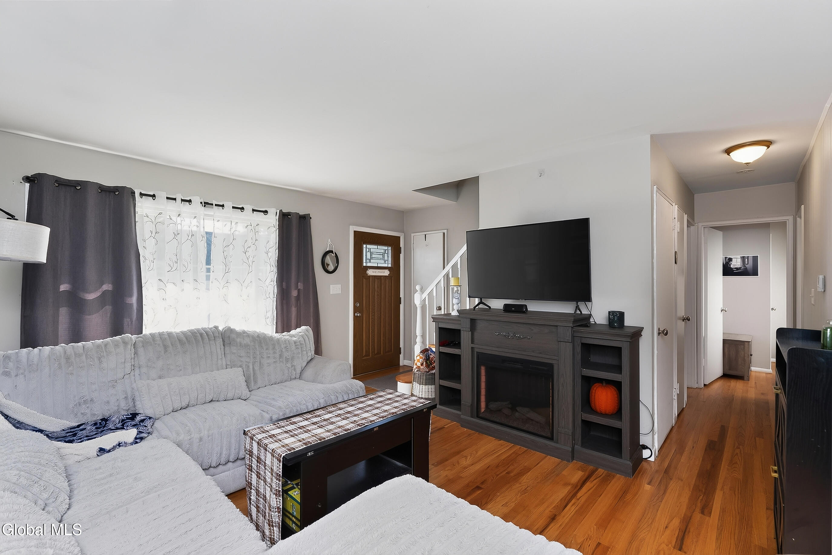 Living room with a light sectional, hardwood floors, and a television above a dark fireplace mantel.