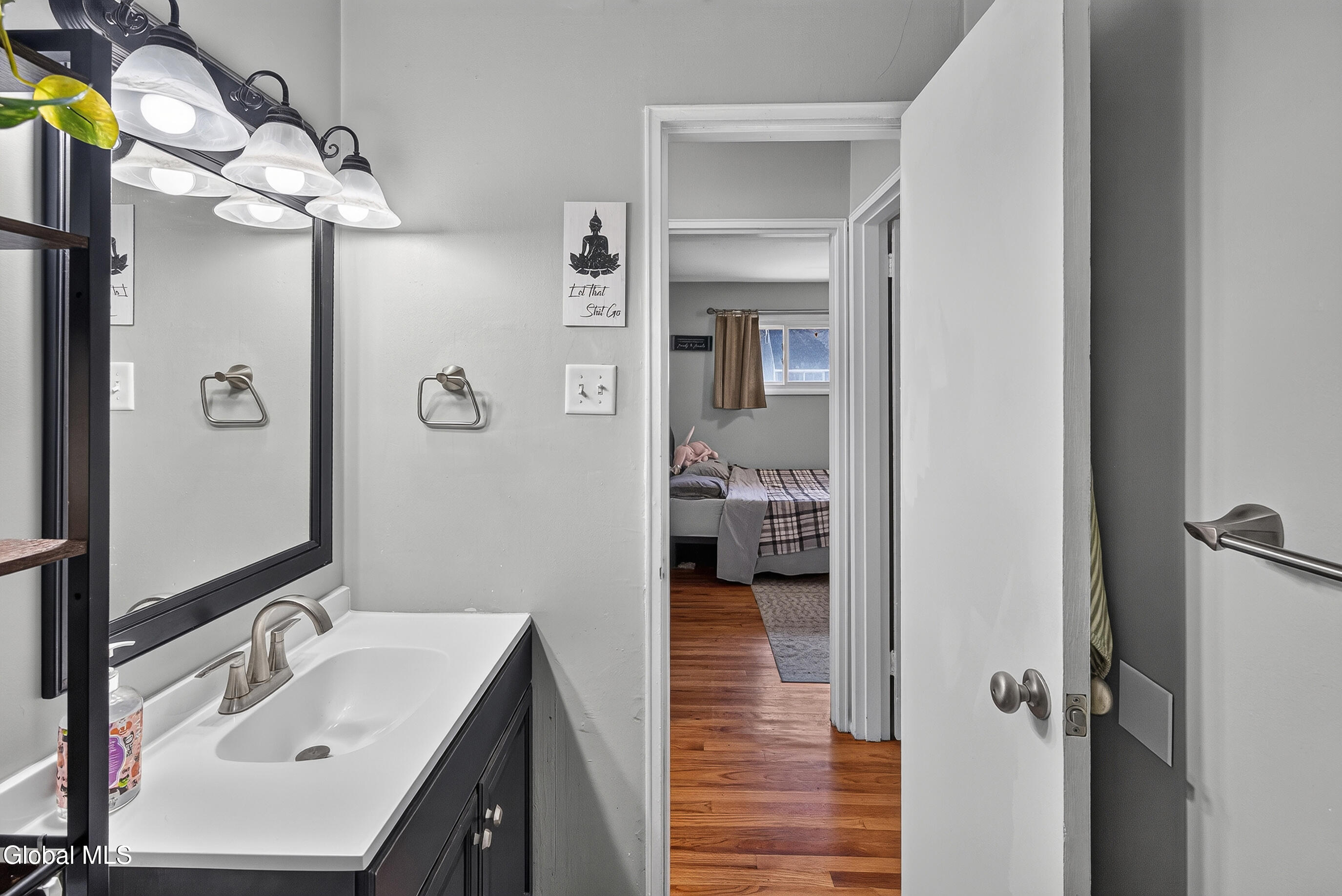 Bathroom vanity and mirror overlooking a bedroom with hardwood floors.