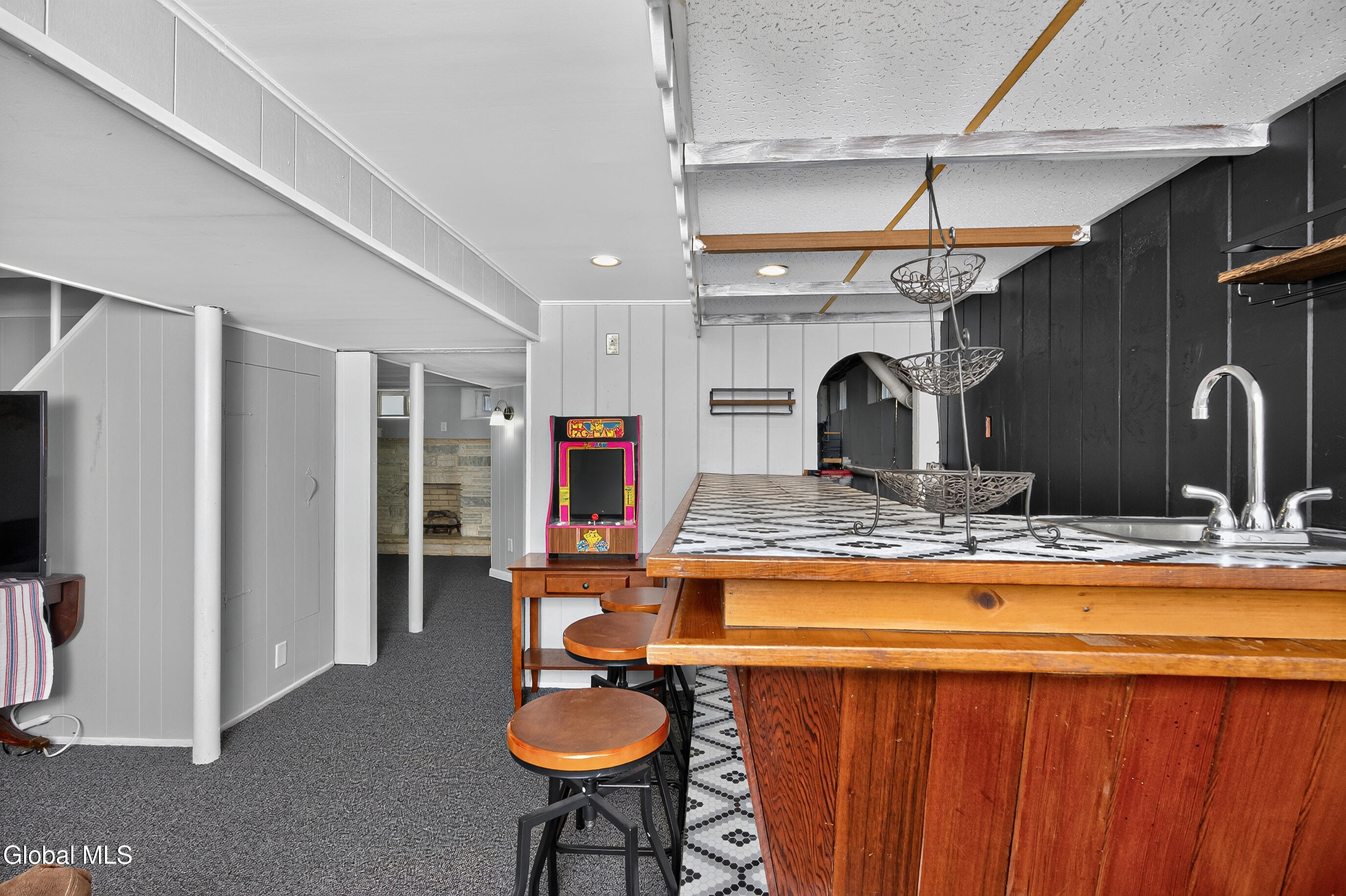 Basement recreation room with a wood bar, tiled counter, arcade game, and stone fireplace.