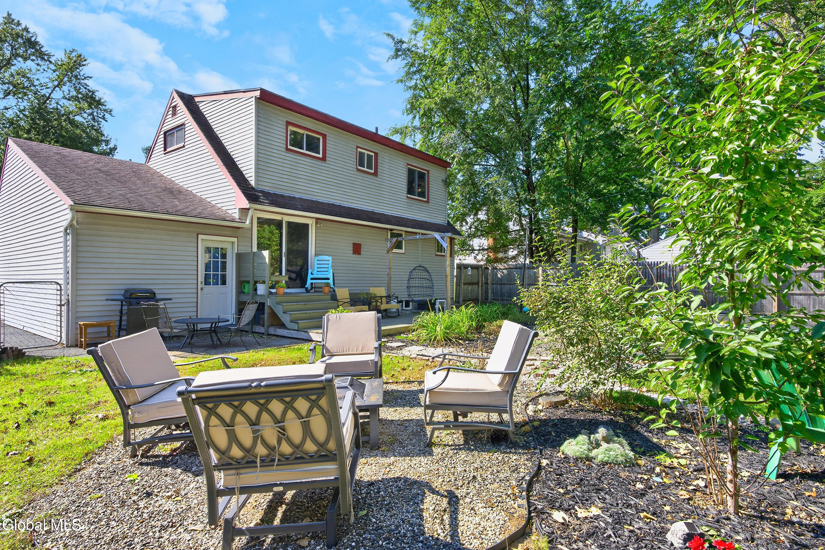 Rear of a two-story home with a raised deck and furnished gravel patio.