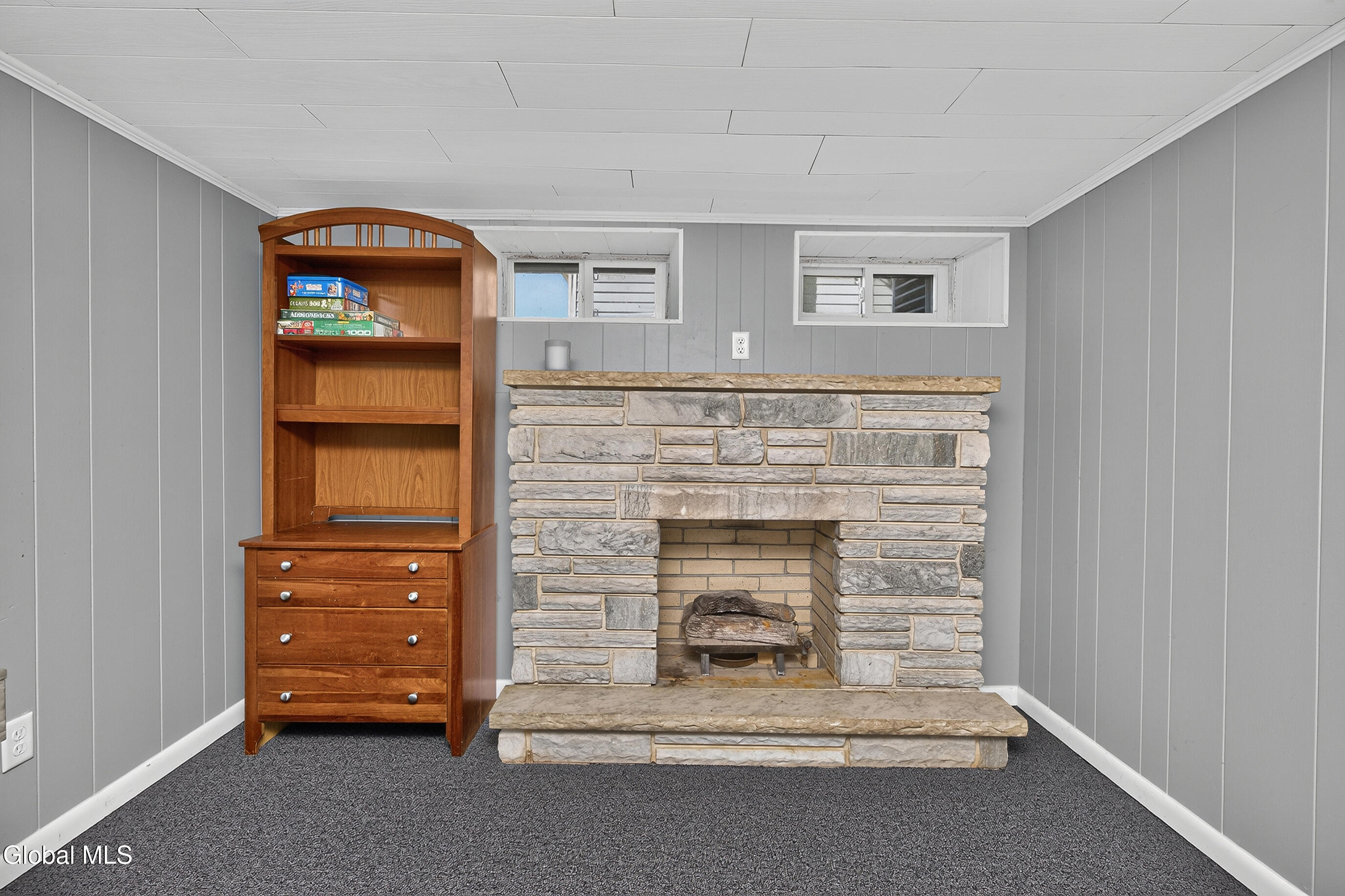 Basement with a stone fireplace, gray paneled walls, and a wooden shelving cabinet.