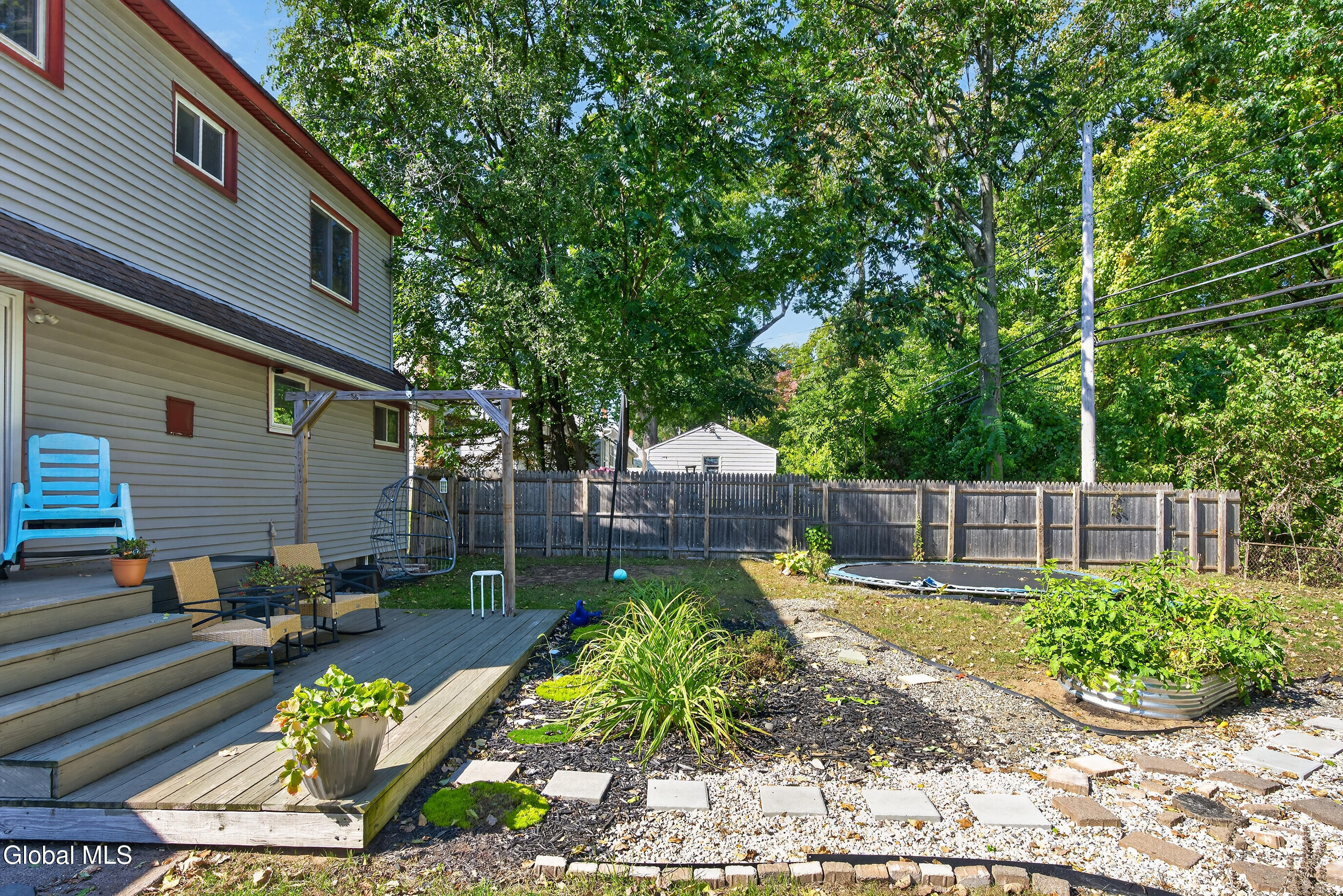 Backyard with a raised deck, fenced garden, and round trampoline beside a two-story home.