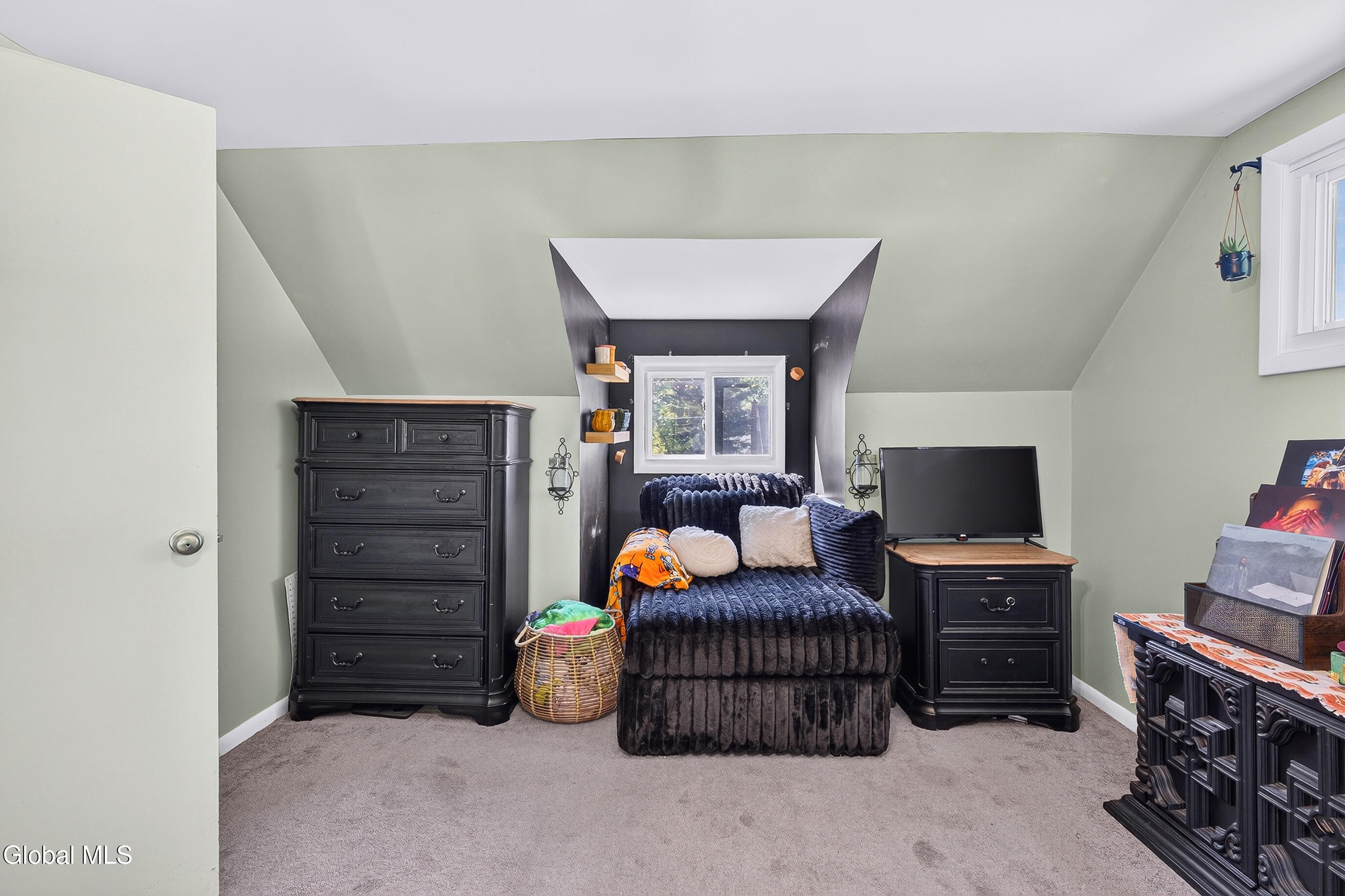 Attic bedroom with sloped ceilings, a dark bed under a recessed window, and matching dark dressers.