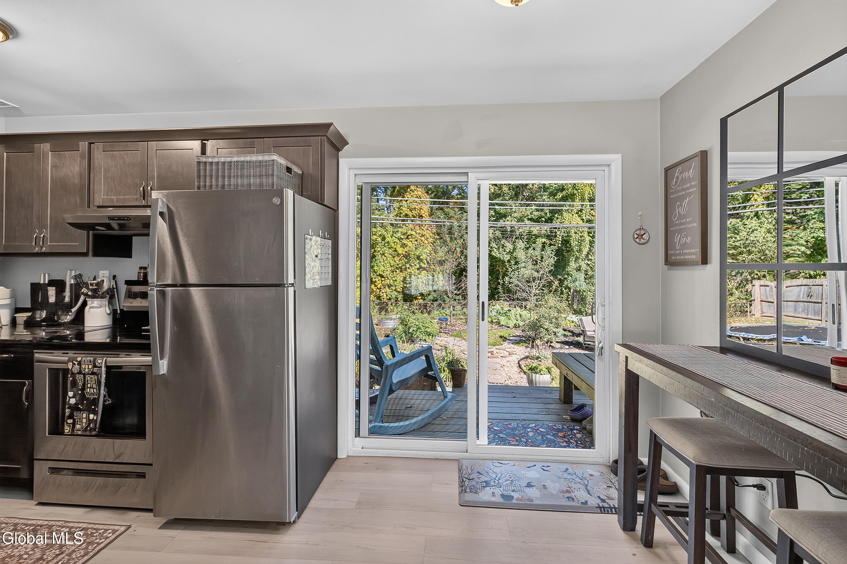 Kitchen with dark cabinets and stainless appliances, opening through sliding doors to a deck and leafy backyard.
