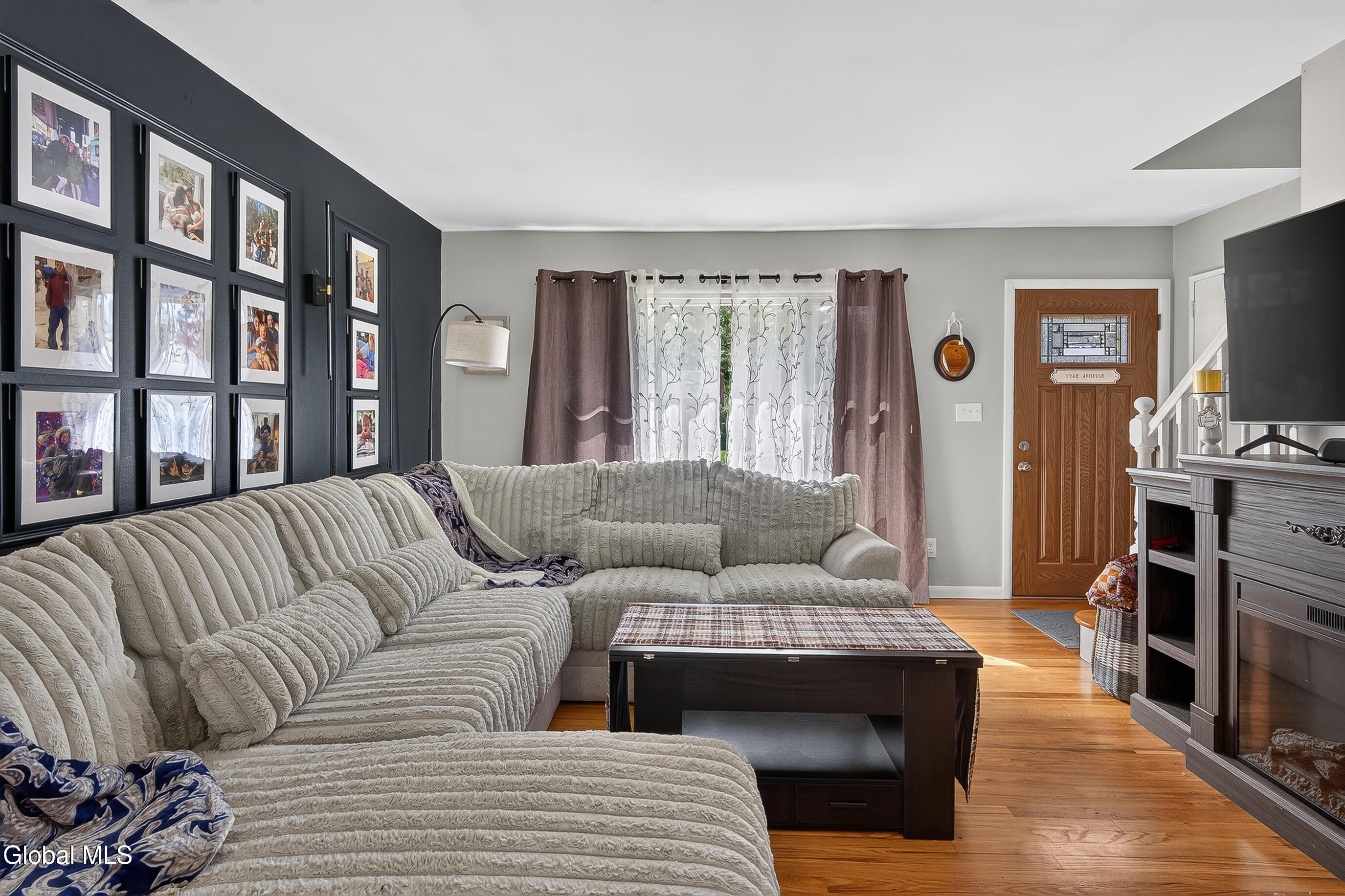 Living room with a cream sectional, family photo gallery wall, hardwood floors, and a fireplace.