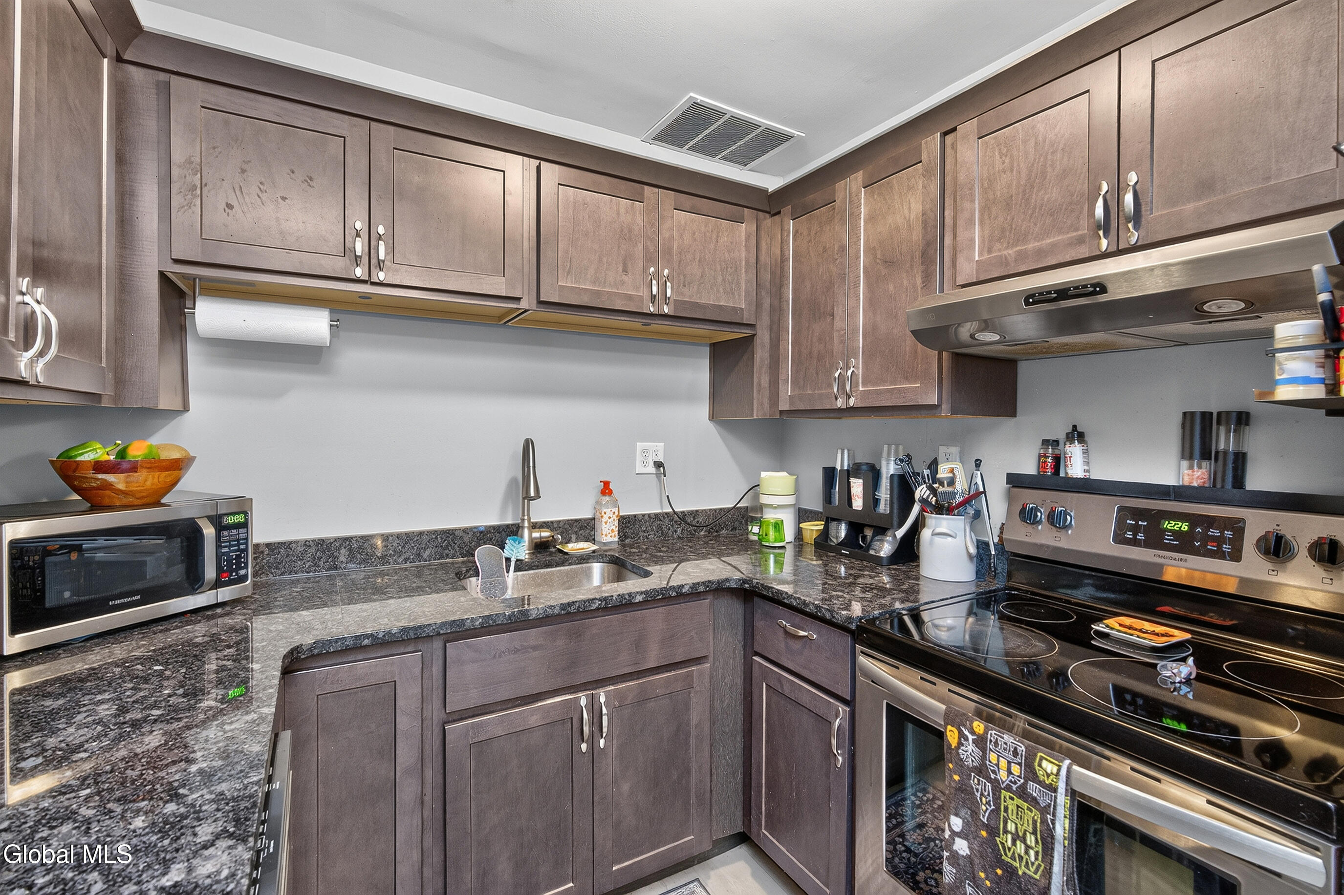 Kitchen with dark wood cabinets, granite countertops, and a black electric range.