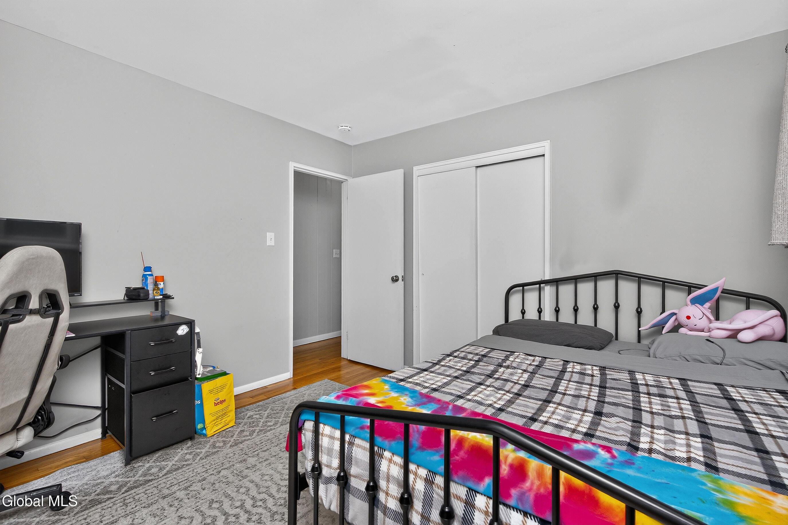 Bedroom with a black metal bed, plaid comforter, colorful tie-dye blanket, and computer desk.